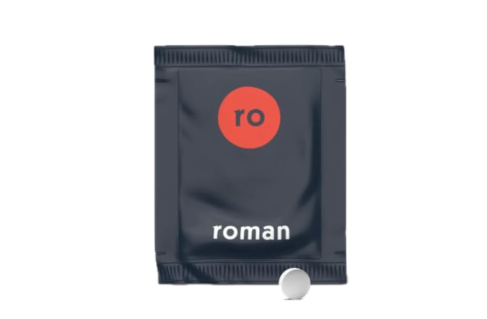 A grey and red individual use packet of a Roman dietary supplement with a white tablet in front of the packet.